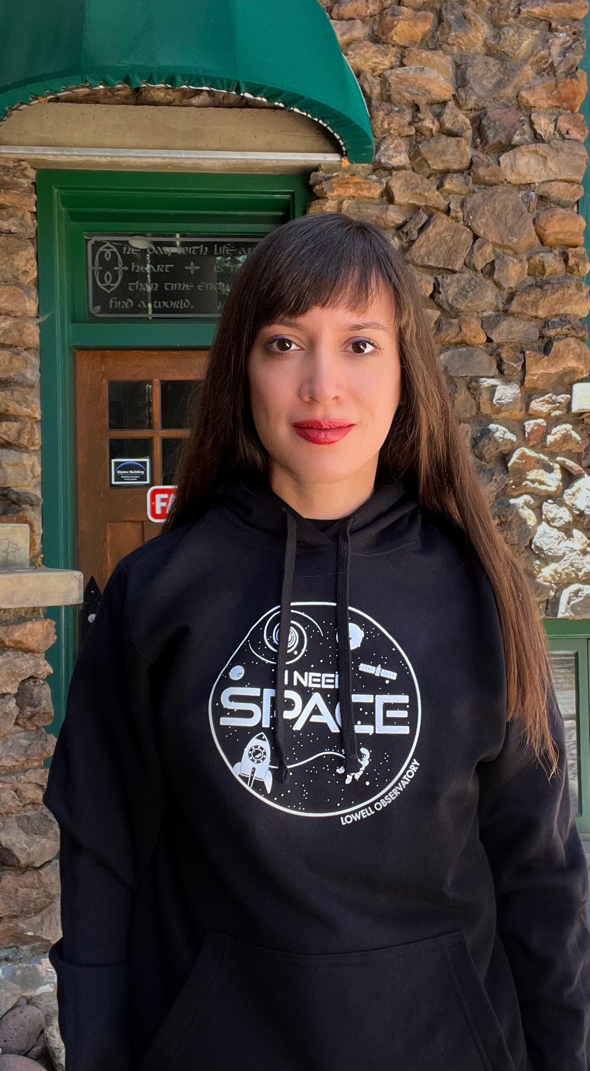 Brunette female wearing black hoodie with white text that reads, "I Need Space." She is standing near Lowell Observatory's historic Rotunda building.