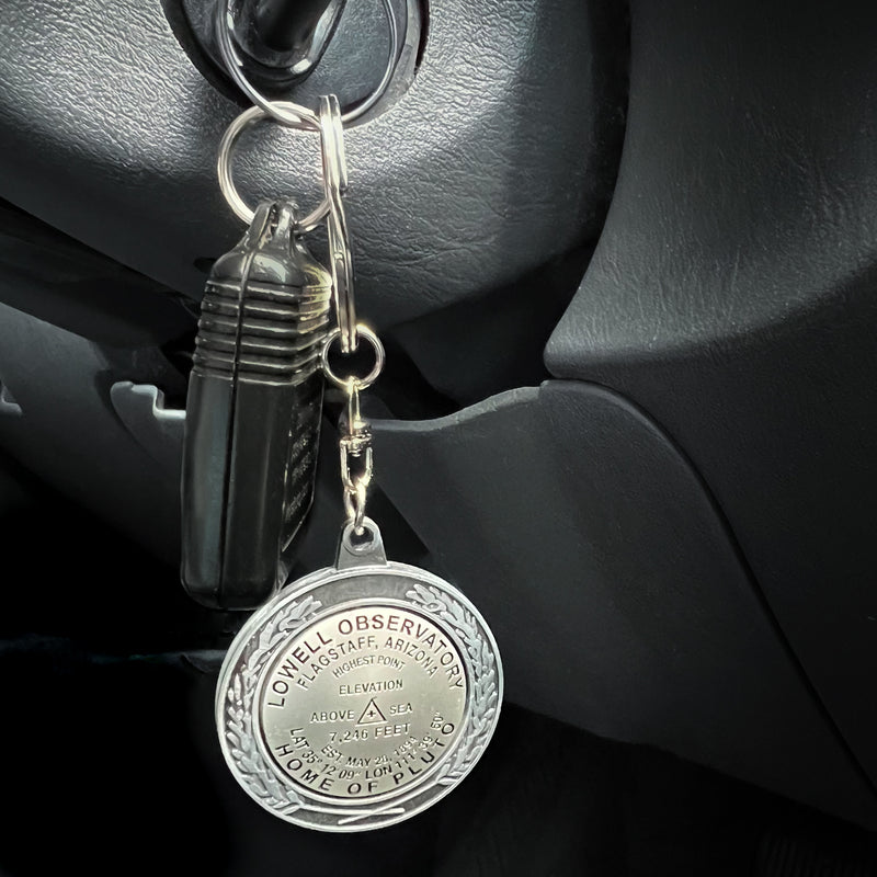 Lowell Benchmark Keychain attached to a key that is inserted into the ignition of an upscale SUV with a dark grey interior.