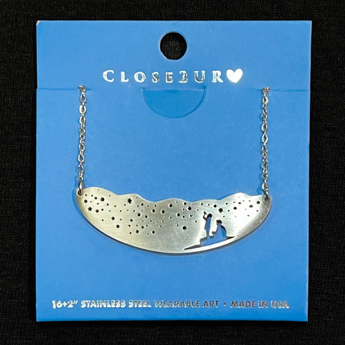 Stainless steel necklace showing starry nightscape and silhouette of two individuals gazing upward at the sky.