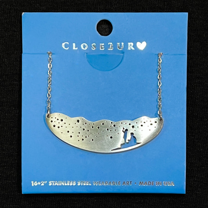 Stainless steel necklace showing starry nightscape and silhouette of two individuals gazing upward at the sky.